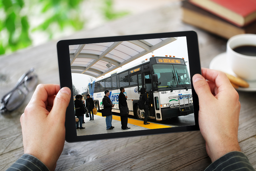 Person holding an iPad showing a picture of people boarding an Xpress bus