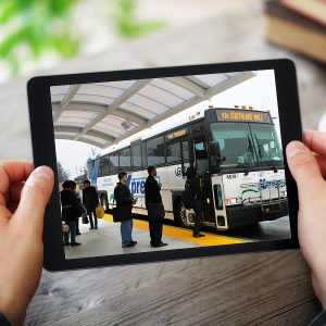 Person holding an iPad showing a picture of people boarding an Xpress bus