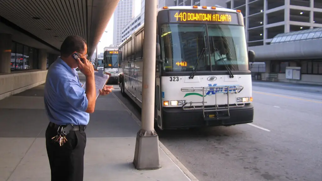 xpress GRTA bus operator outside bus, standing on sidewalk, talking on a cell phone