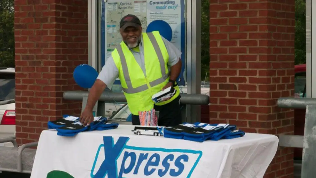 Picture of an xpress GRTA team member at a sign-up booth smiling for the camera